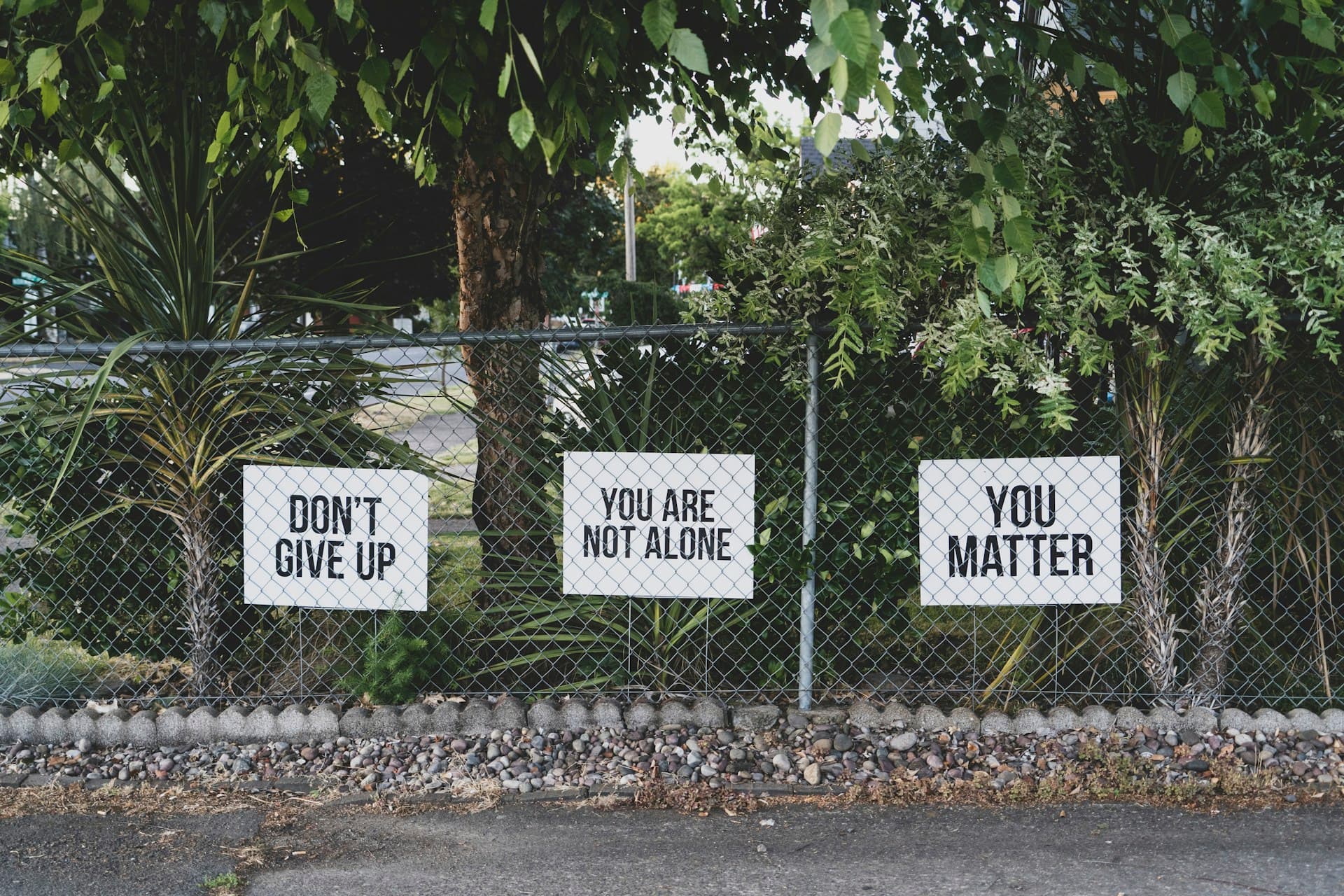 Hand-painted signs on a fence reading encouragement messages about mental health and support.